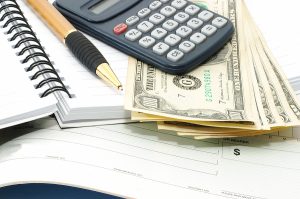 Note pad with pen, calculator and cheque book and cash. Check book.