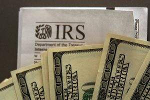 hundred dollar bills fanned out over an IRS envelope metaphor for paying taxes or getting a refund